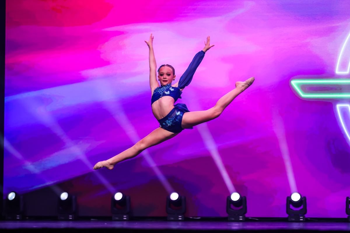 A dancer in a sequined costume in a split leap against pink light