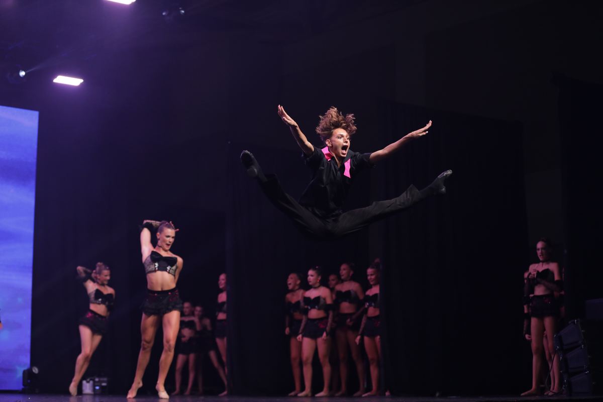 A dancer leaping high above a group on a dark stage