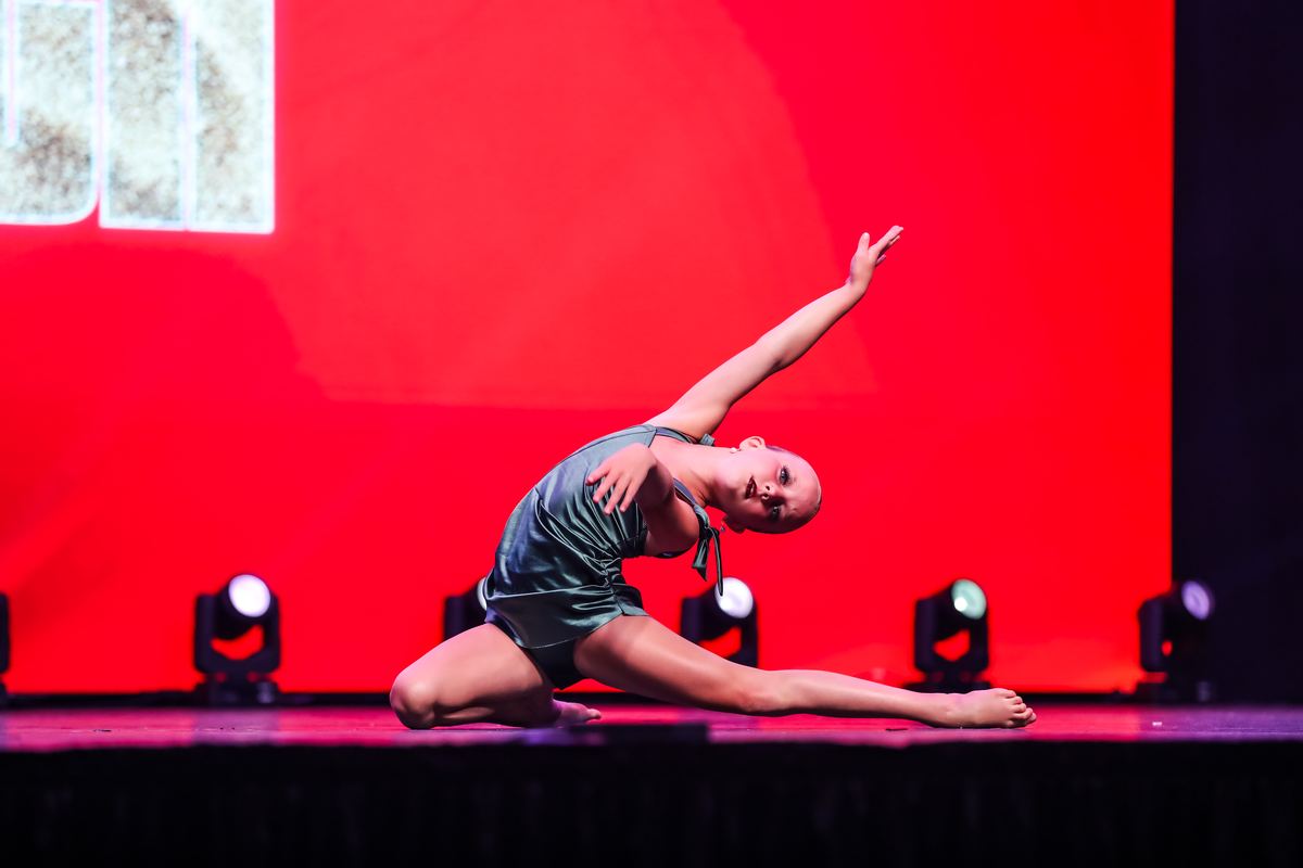 A soloist stretched low on the floor against a red backdrop